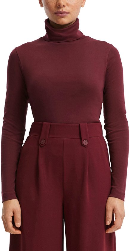 Een bordeauxrode coltrui met lange mouwen, gedragen onder een broek met hoge taille.