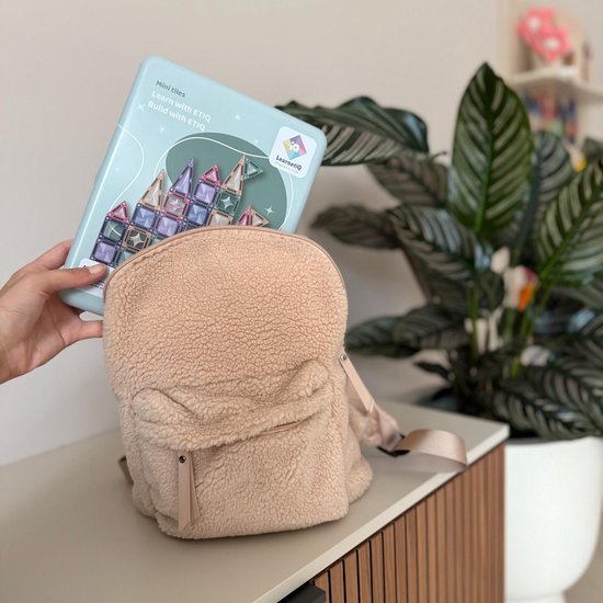 Een hand houdt de pastelkleurige LearnetiQ reisset boven een teddy rugzak.