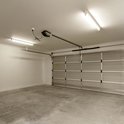 Een garage met betonnen vloer, garagedeur en twee tl-verlichtingsarmaturen.