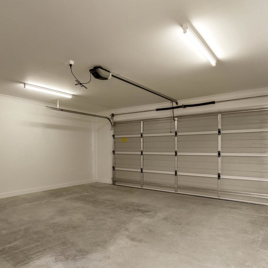 Een garage met betonnen vloer, garagedeur en twee tl-verlichtingsarmaturen.