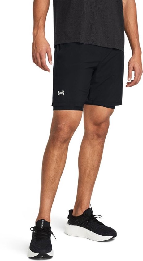 Man in een zwarte sportbroek met reflecterend Under Armour logo op de linkerbroekspijp.