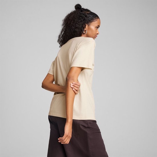 Model draagt een lichtbeige PUMA T-shirt en donkere broek, gedraaid naar de zijkant.
