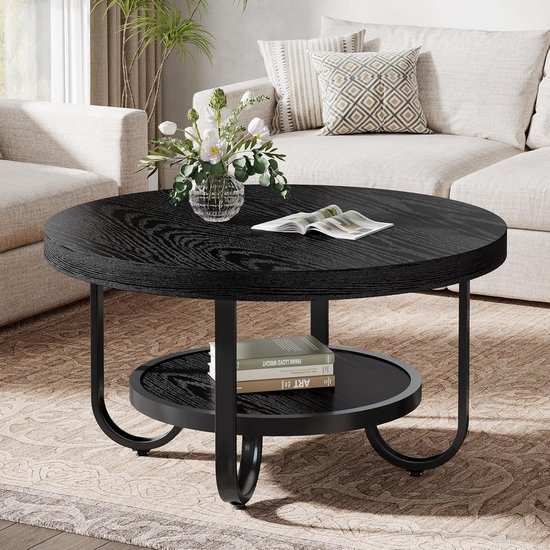 Zwarte ronde salontafel met een opbergplank, met een vaas bloemen en een open boek bovenop.