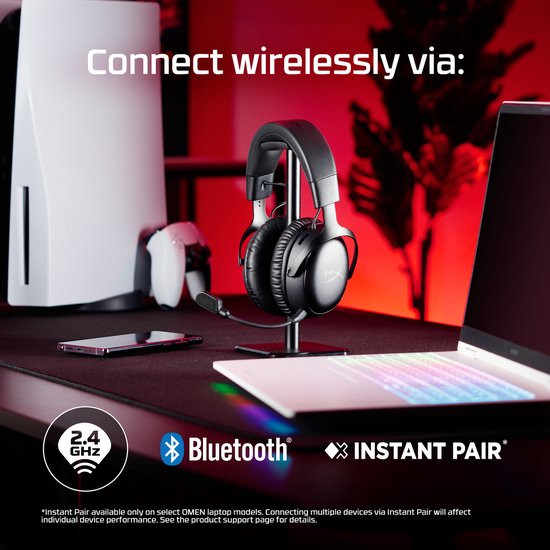 Zwarte HyperX gaming headset op een standaard, met PlayStation 5 en laptop op de achtergrond.