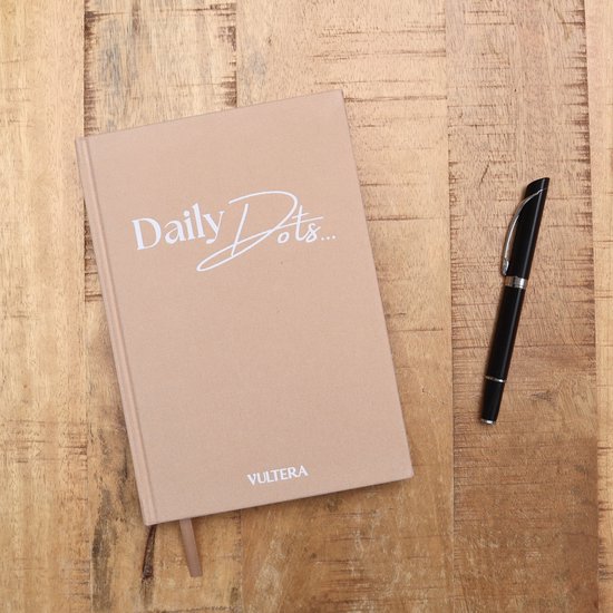 Beige notitieboek "Daily Dots..." met pen op houten tafel. Afmetingen 21x15cm.