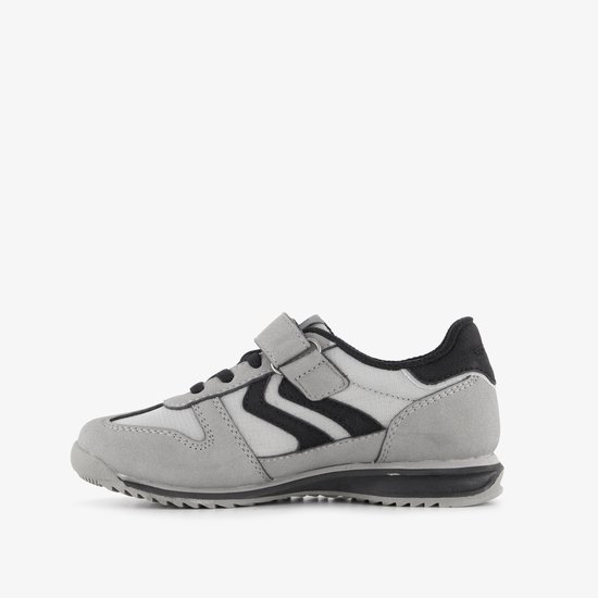 Grijze sneaker met zwarte zigzagstrepen, klittenbandsluiting en zwarte accenten.