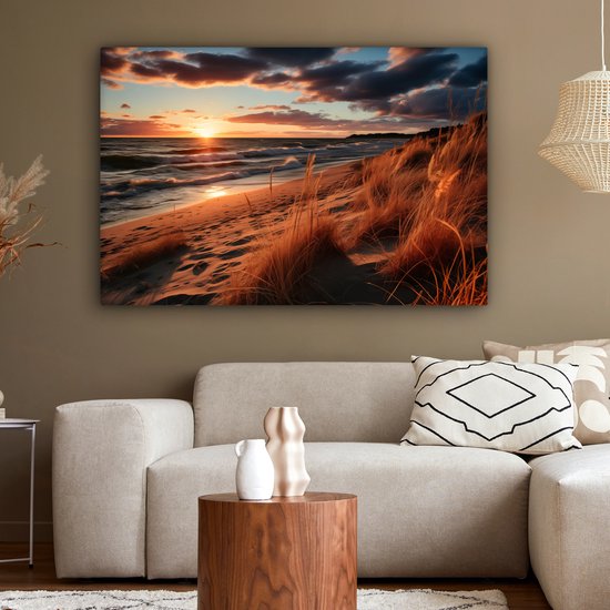 Une toile représentant un coucher de soleil sur une plage avec dunes et oyats, au-dessus d'un canapé de salon.