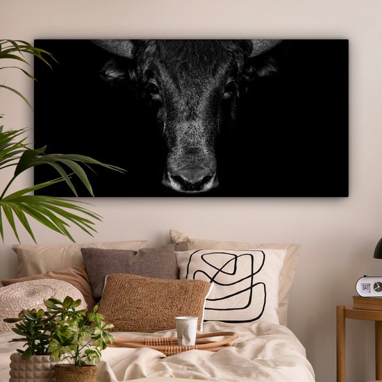 Tête de taureau sur toile noir et blanc, centrée au-dessus d'un lit avec des coussins.