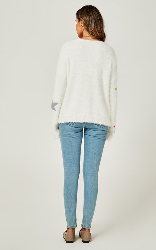 Achterkant van model in witte, pluizige trui met veelkleurige sterrenprint op de mouwen. Blauwe jeans.