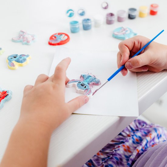 Kind schildert een blauw figuurtje van Stitch met een kwast en verf.