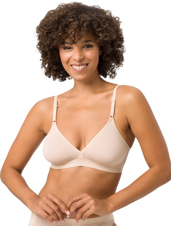Model draagt een beige beugelvrije BH en slipje, met krullend haar, kijkt glimlachend naar de camera.