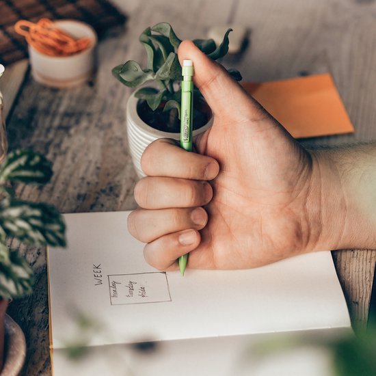 Hand houdt een limegroen BIC ECOlutions vulpotlood vast boven een open notitieboekje.