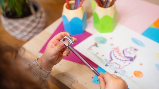 Kind dat een Bic potlood slijpt met een metalen puntenslijper boven een kinder tekening.