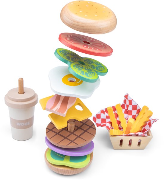 Hamburger jouet en bois en morceaux, flottant les uns sur les autres avec pain, laitue, tomate, œuf, fromage, bacon, oignon violet. Frites et tasse à côté.