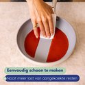 Hand met gouden ring veegt rode saus uit een grijze koekenpan met witte rand.