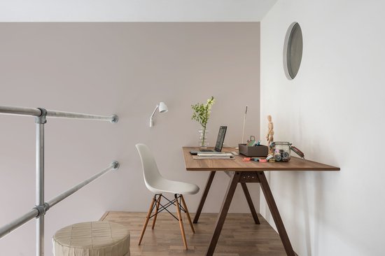 Een houten bureau met een laptop, plant en kantoorbenodigdheden, met een witte stoel, een ronde poef en een metalen leuning.