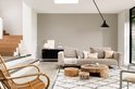 Woonkamer met beige bank, houten tafels en een rieten stoel.