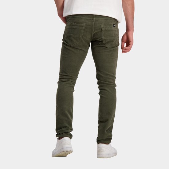 Man met groene corduroy jeans, zwarte sneakers en witte sokken, van achteren gezien.