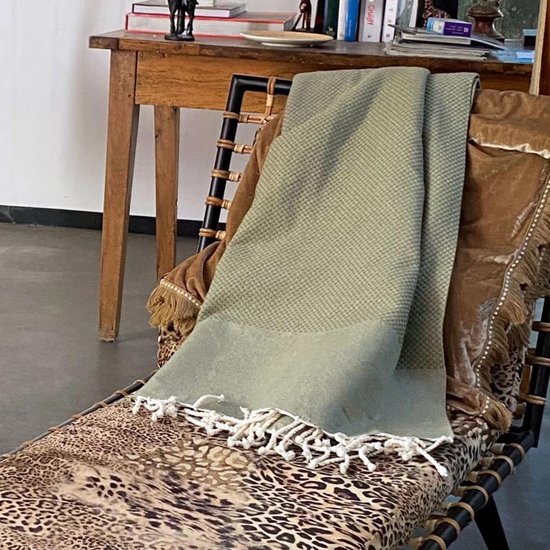 Olijfgroen wafel plaid met franjes, gedrapeerd over een ligstoel met luipaardprint kussen en bruine fluwelen deken.