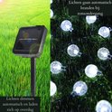 Lichtsnoer met transparante lichtballetjes, koud wit. Solar paneel in groen gras en verlichte lichtjes in de regen.