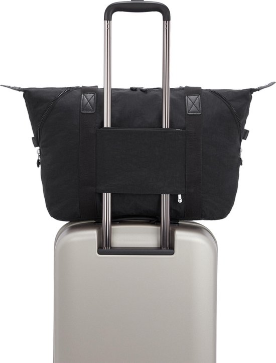 Sac Kipling ART M noir avec poignées et passant pour trolley, sur une valise argentée.