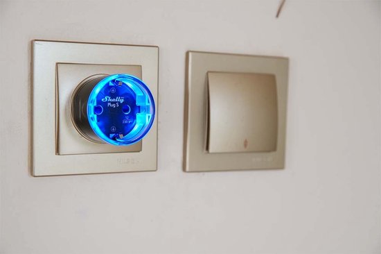 Blauwe Shelly Plug S in een stopcontact naast een schakelaar.