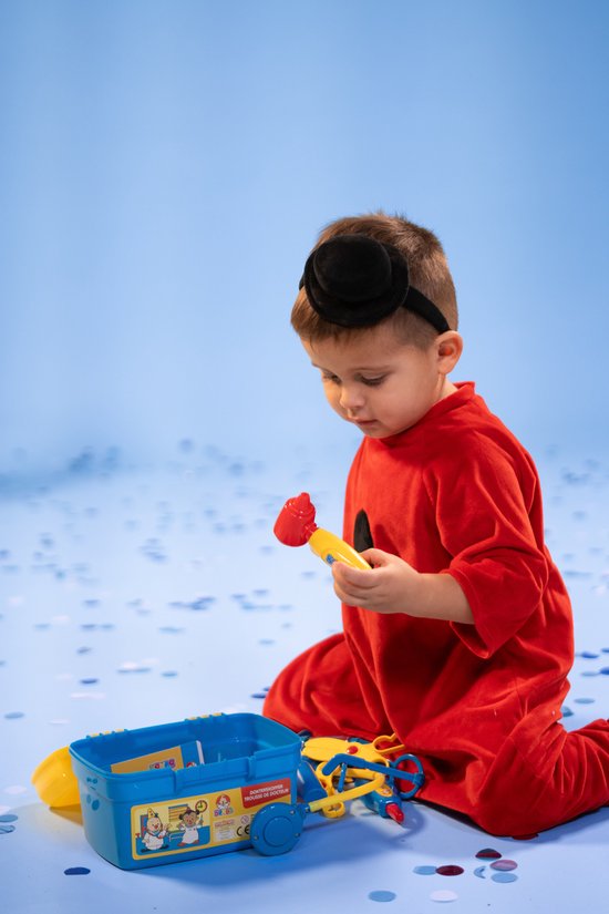 Jongen in rood kostuum met zwarte hoed, speelt met dokterskoffer en speelgoed.