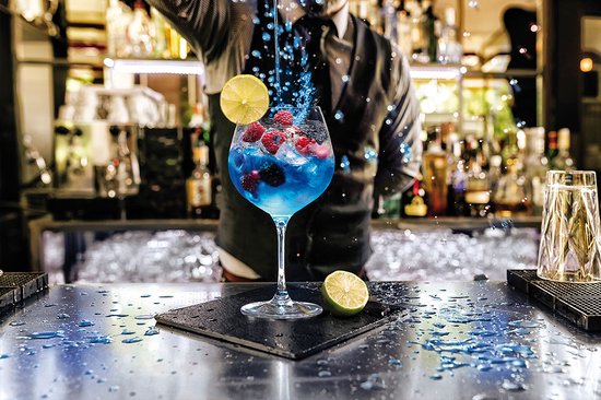 Cocktail bleue dans un verre à vin avec framboises, myrtilles et une rondelle de citron.
