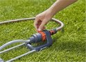 Hand verstelt oranje connector op Gardena zwenksproeier op gras.
