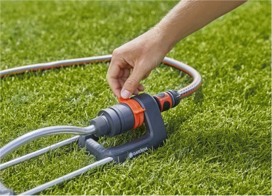 Hand verstelt oranje connector op Gardena zwenksproeier op gras.