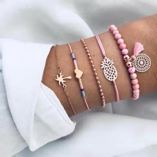 Damesarm opgemaakt met vijf armbanden: roze kralen, hartje, palmboom, ananas en gouden balletjes.