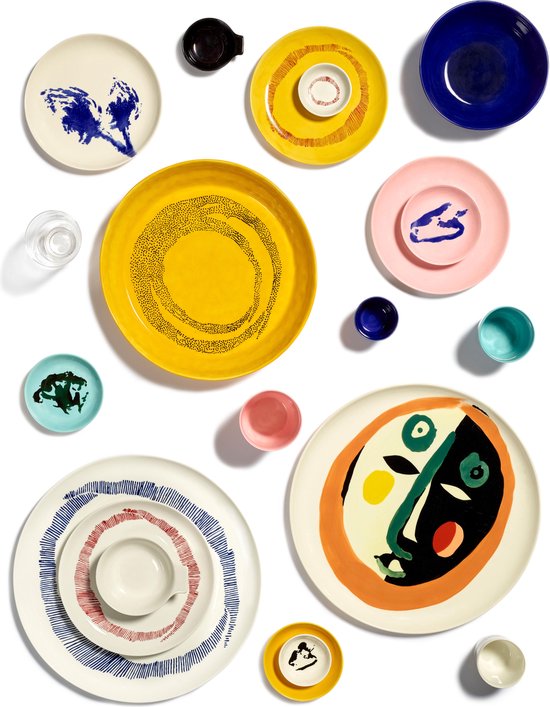 Verschillende gekleurde borden, kommen en mokken op een witte achtergrond, waaronder twee grote schalen met gezicht-motieven.