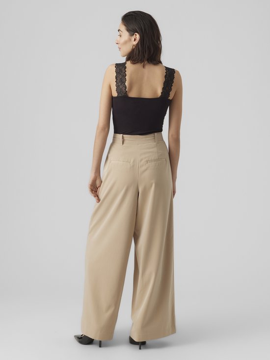 Model van achteren gezien, draagt een zwarte top met kanten bandjes op de schouders en een beige wijde broek.