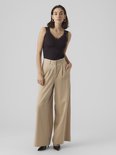 Model in zwarte top met kanten randje aan de halslijn, gecombineerd met een beige wijde broek.