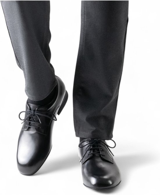 Chaussures derby noires et cuir lacées, portées par un homme en pantalon gris.