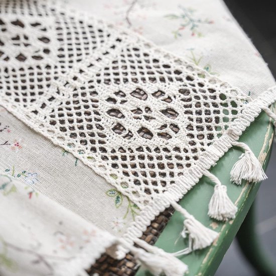 Detail van kanten inzetstuk met kwastjes op beige linnen vitrage.