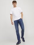 Man met een witte t-shirt en een slim fit jeans in denimblauw. De jeans heeft een lichte wassing en bruine naden.