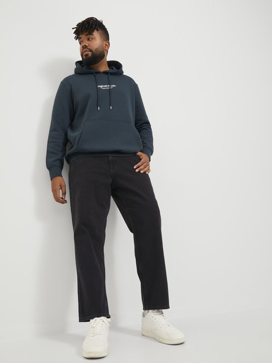 Man in donkergroene hoodie met tekstprint en donkergrijze jeans.