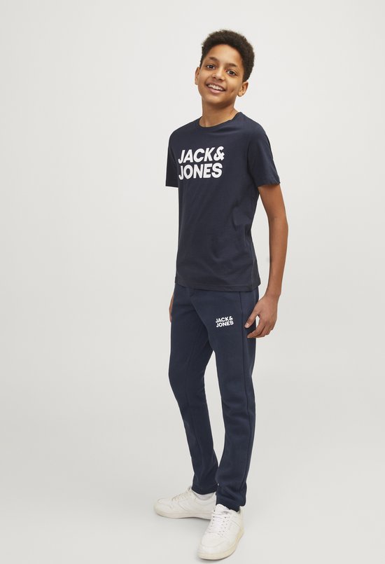Jongen staand in een marineblauwe joggingbroek en T-shirt met 'JACK & JONES' opdruk, met witte sneakers.