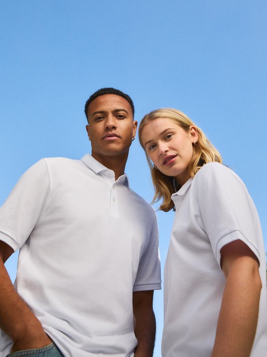 Man en vrouw van dichtbij, beiden dragen witte polo shirts, tegen een blauwe hemel.