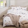 Wit dekbedovertrek met paars- en bruinbloemenpatroon, met beige plaid en een knoestige poef.