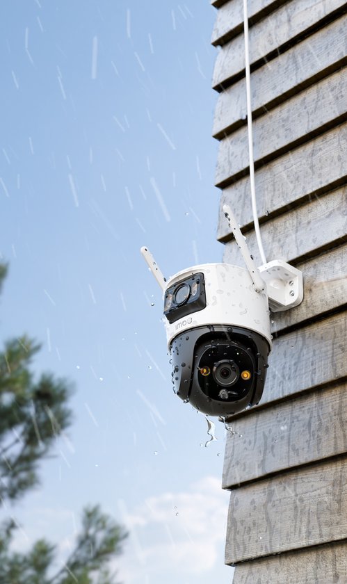 Witte en zwarte Imou beveiligingscamera met dubbele lens, gemonteerd aan een houten muur in de regen.
