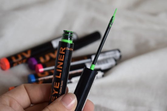 Hand die een zwarte eyeliner tube met 'UV EYE LINER' vasthoudt. Groen neon product is zichtbaar op de applicator.