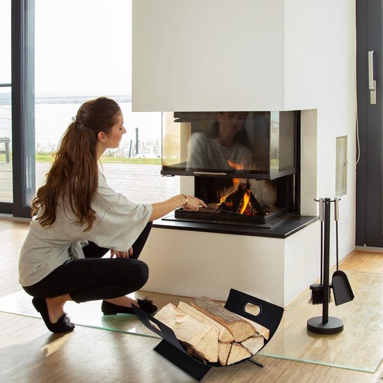 Vrouw bij open haard die hout in zwarte houtmand legt.