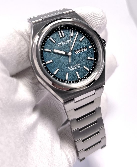 Zilverkleurig Citizen Eco-Drive Titanium horloge met een gestructureerde blauwgroene wijzerplaat en datumweergave.