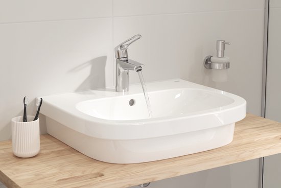 Witte wasbak met houten aanrechtblad, chromen kraan en zeepdispenser.