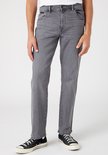 Man in donkergrijze straight-fit jeans, staand met zwarte sneakers.