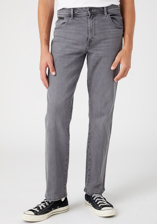 Man in donkergrijze straight-fit jeans, staand met zwarte sneakers.