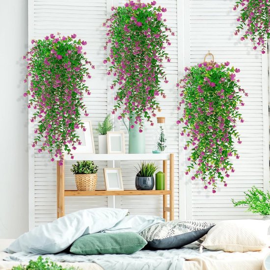 Drie hangende planten met roze bloemen en groene bladeren, decoratief gehangen in een kamer met een open kast.