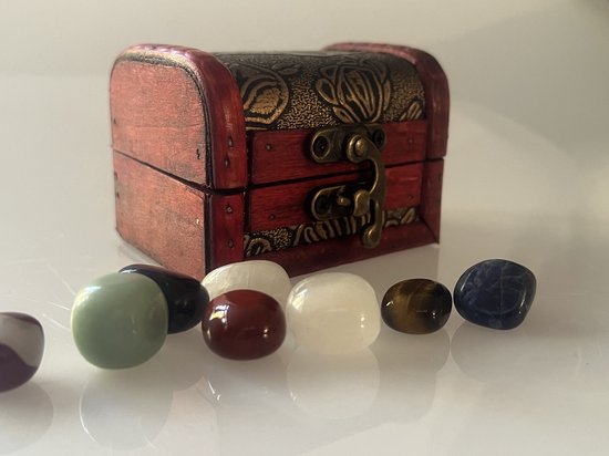 Un coffre au trésor en bois avec des ornements dorés. Devant le coffre se trouvent sept pierres polies : rayée rouge et blanche, verte, brune, blanche, rouge, bleue, blanche.
